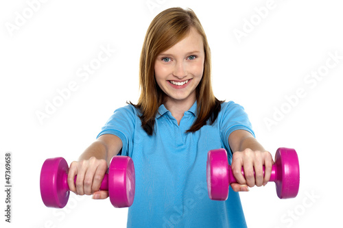 Adorable teen holding dumbbells in her outstretched arms