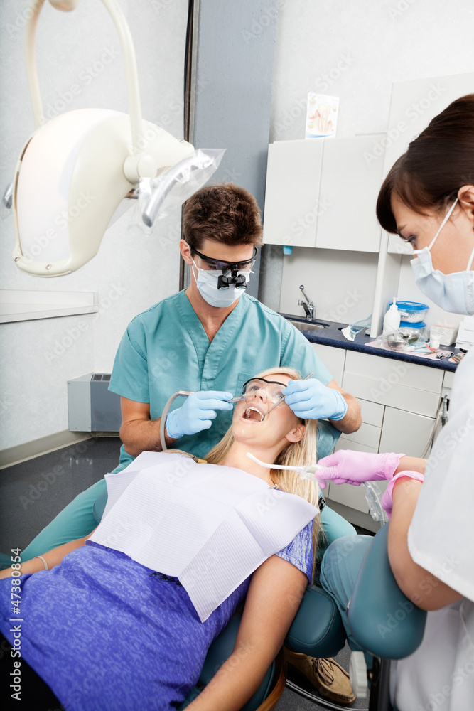 Dentist And Female Assistant Treating A Patient At Clinic Dentist And Female Assistant Treating A Patient At Clinic