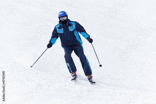Man in darkblue ski suit glides downhill on skis