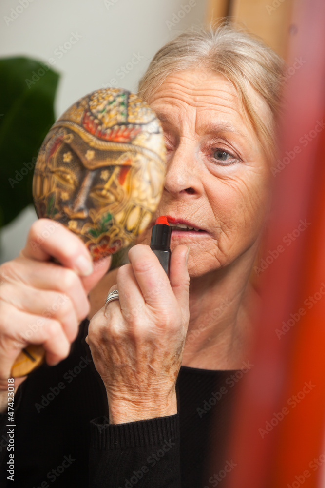 Fototapeta premium Good looking senior woman doing make-up in front of mirror.