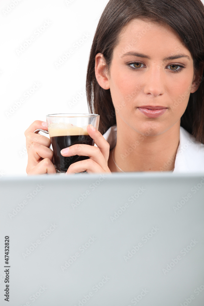 Woman drinking coffee while working at her laptop Woman drinking coffee while working at her laptop