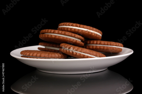 Chocolate cookies with creamy layer on plate isolated on black