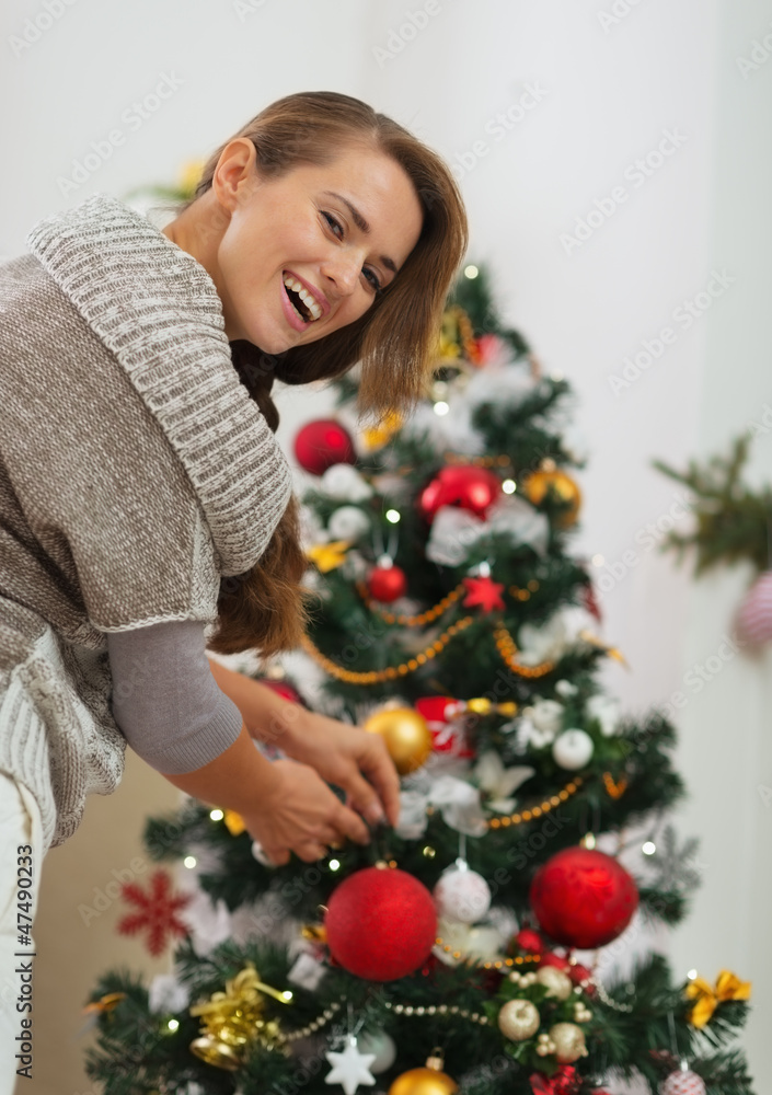 Happy young woman hanging Christmas ball on Christmas tree