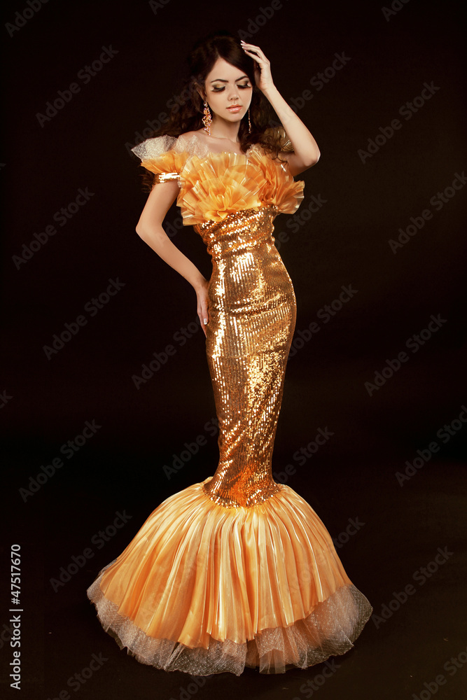 Fototapeta premium Young brunette lady in golden gorgeous dress posing on black bac