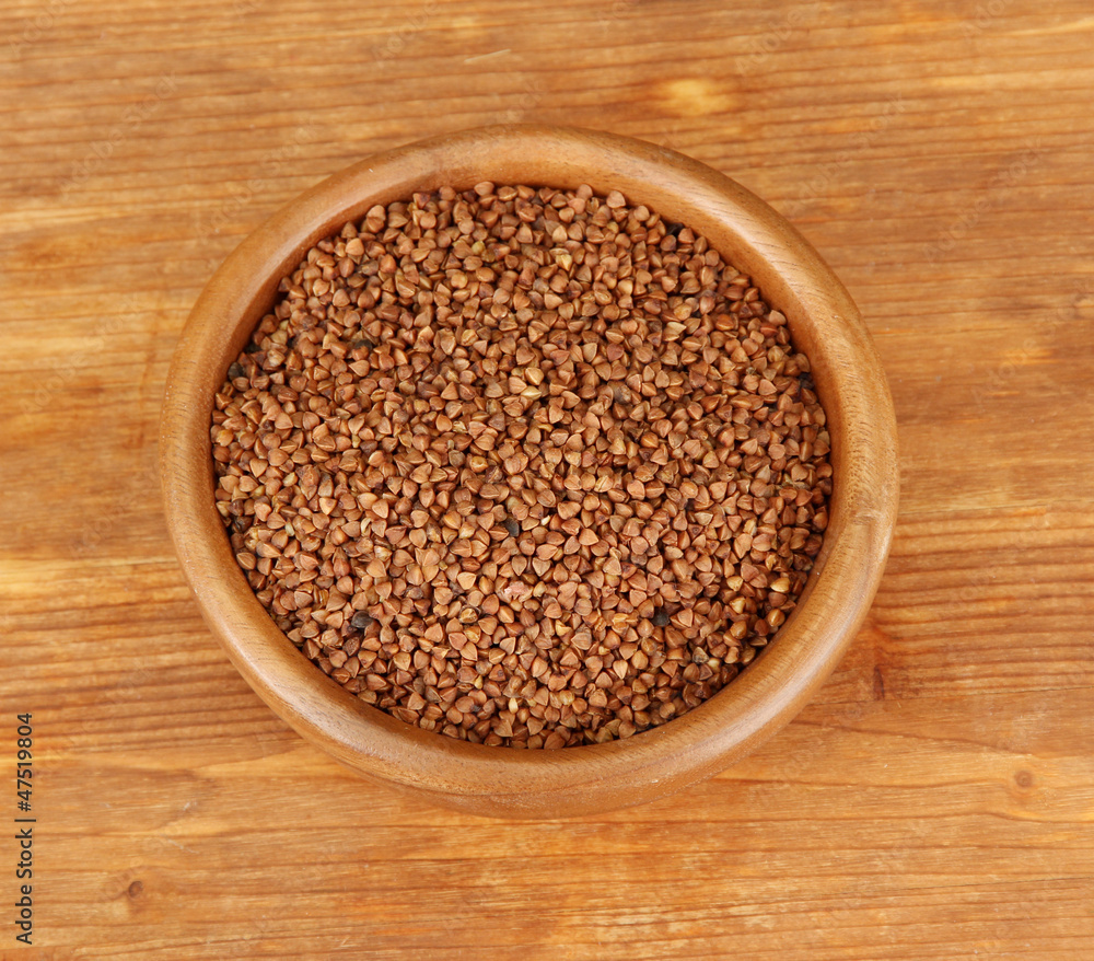 Raw buckwheat in wooden bowl on wooden background Raw buckwheat in wooden bowl on wooden background
