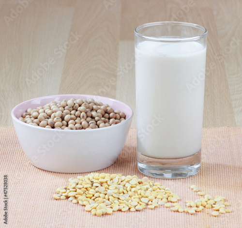 A glass of soy milk with a bowl of raw soybean and seed
