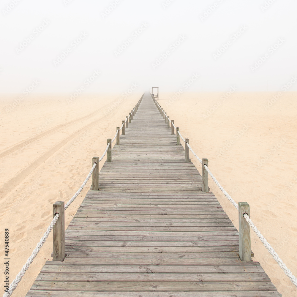 Naklejka premium Wooden footbridge on a foggy sand beach background. Portugal.