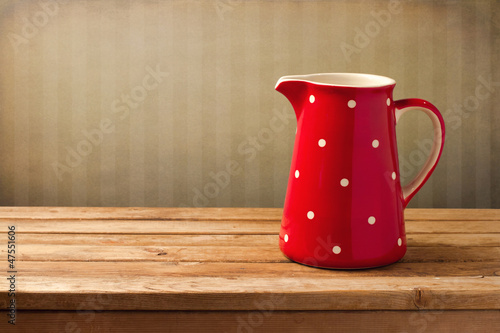 Red jug with dots on wooden table over vintage background