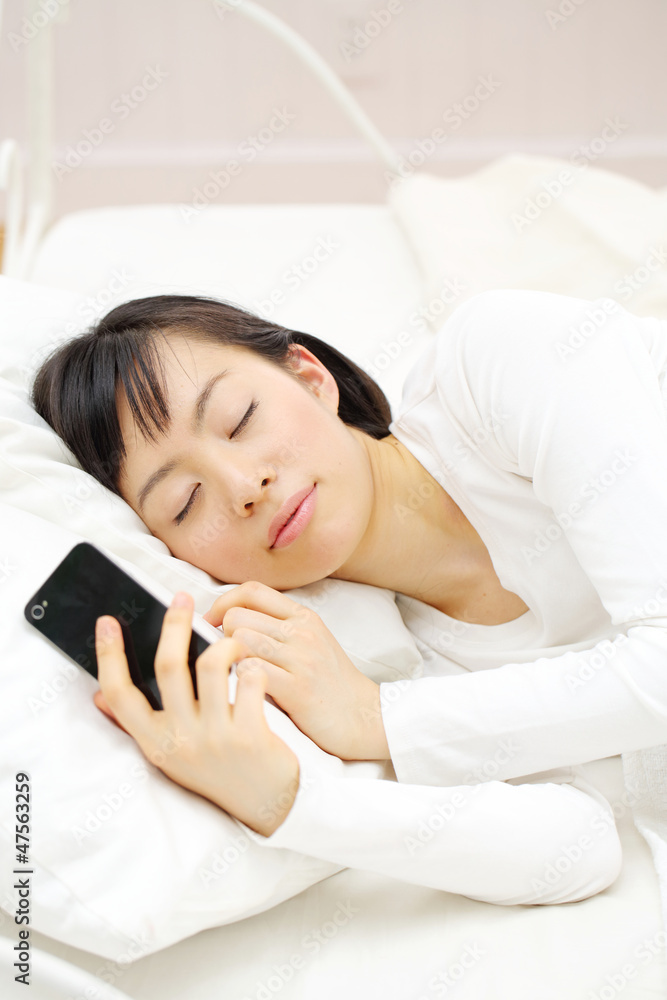 スマートフォンを持ったまま寝る女性 スマートフォンを持ったまま寝る女性