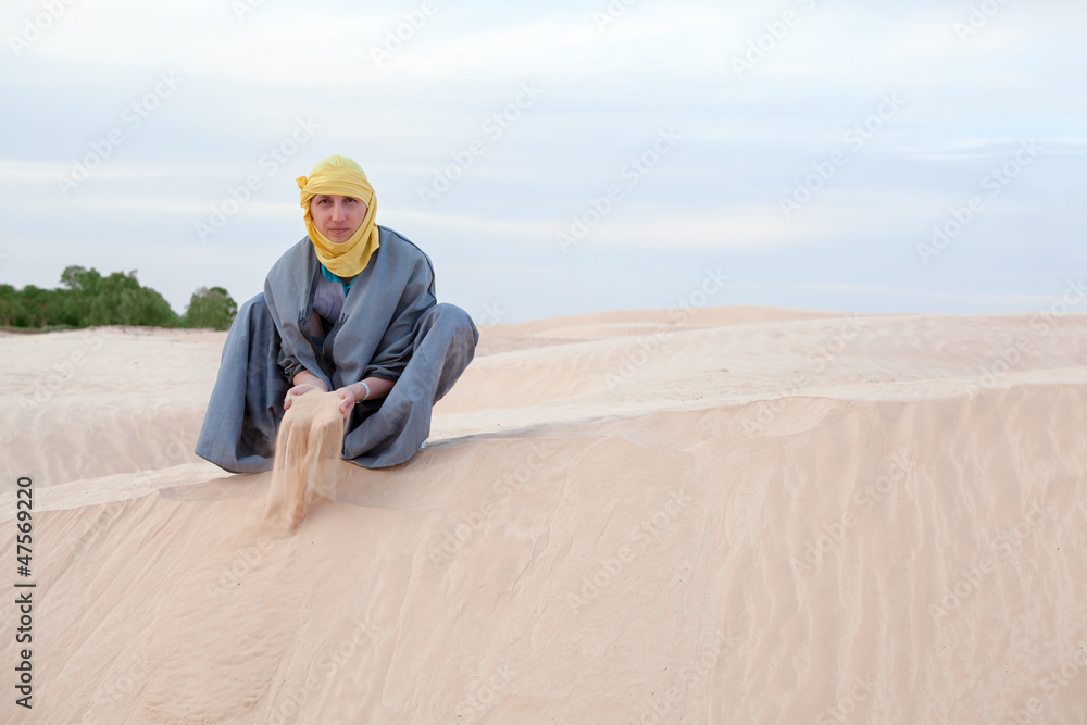 Man in eastern clothes pouring sand by hands on desert
