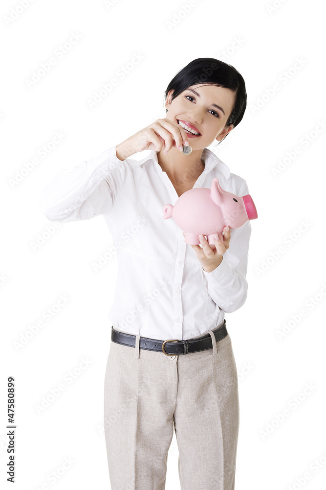 Businesswoman putting a coin into a piggy bank Businesswoman putting a coin into a piggy bank