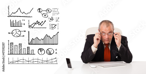 Businessman sitting at desk with diagrams and graphs