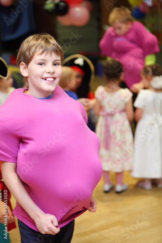 Smiling boy with balloons under pink shirt at children party.