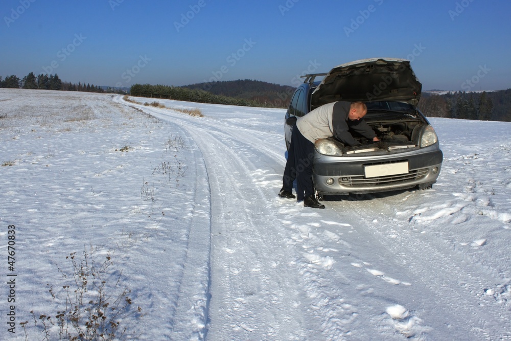 man repairing the car on a deserted road, winter weather