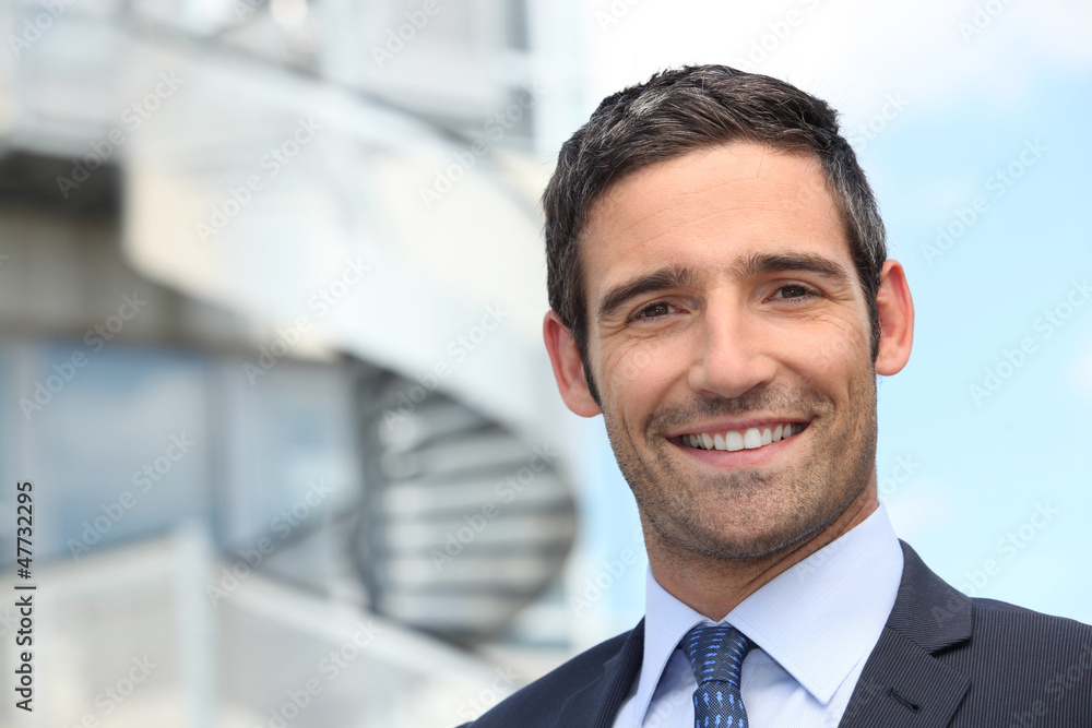 Smiling business man standing outside office building Smiling business man standing outside office building