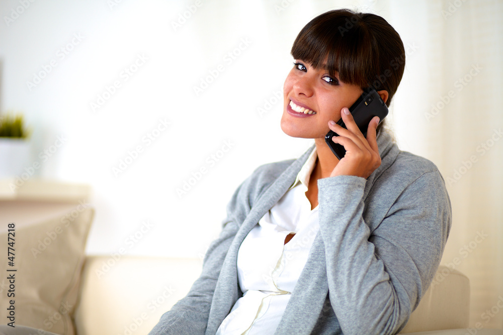 Young woman sitting on sofa speaking at cellphone Young woman sitting on sofa speaking at cellphone