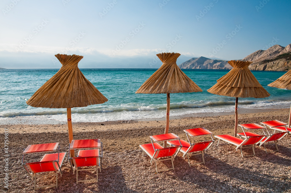 Fototapeta premium Sunshades and orange deck chairs on beach at Baska - Krk - Croat