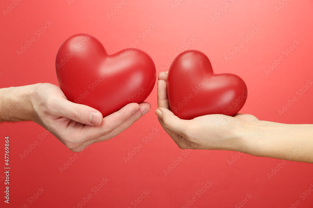 Red hearts in woman and man hands, on red background Red hearts in woman and man hands, on red background