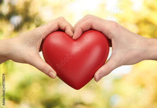 Red heart in woman and man hands  on green background