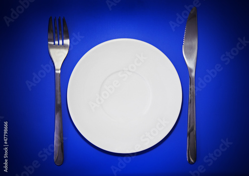 Table serving-knife,plate,fork on colour backdrop.