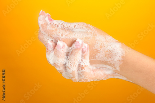 Woman s hands in soapsuds  on orange background close-up