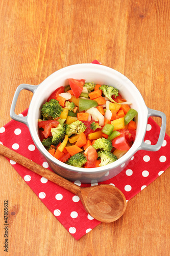 Vegetable stew in gray pot on color napkin on wooden background
