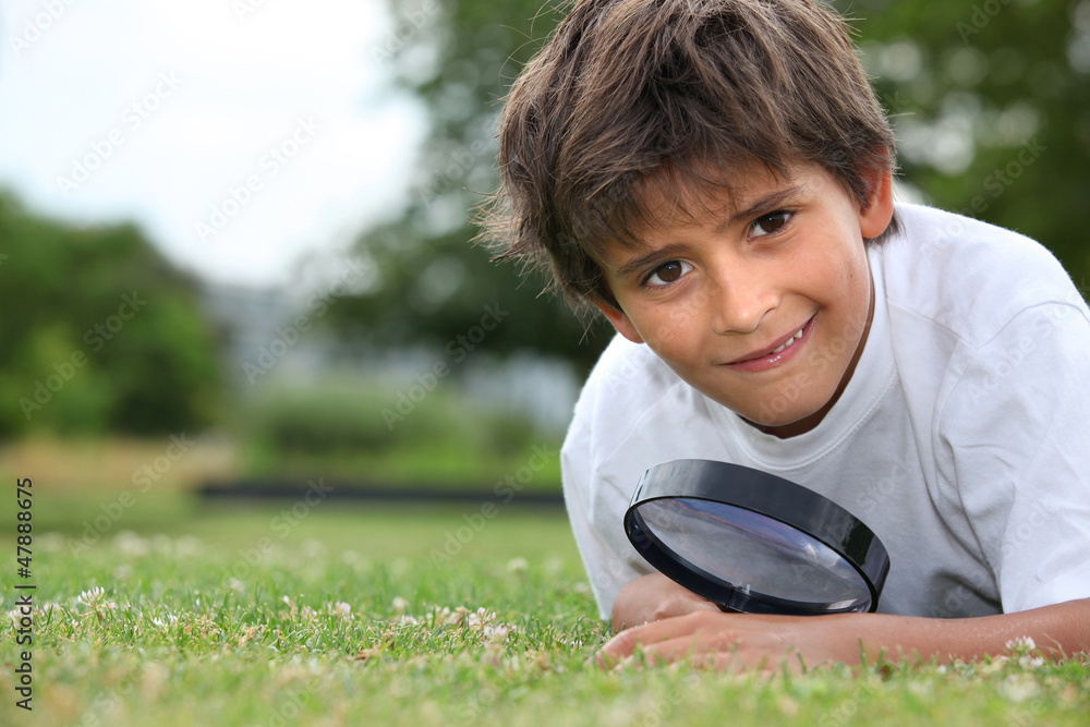 Boy with magnifying glass lying on the grass Boy with magnifying glass lying on the grass