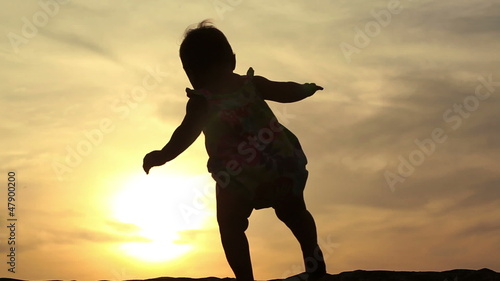 Silhouette of adorable baby girl walking over sunset