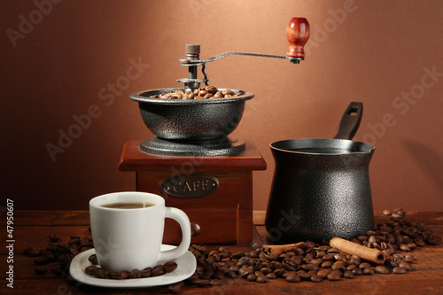 Coffee grinder, turk and cup of coffee on brown background