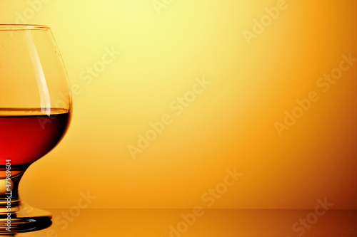 Glass of cognac on yellow background