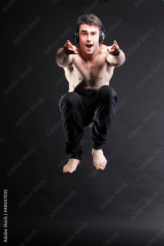 Young man jumping and listening music isolated gray background