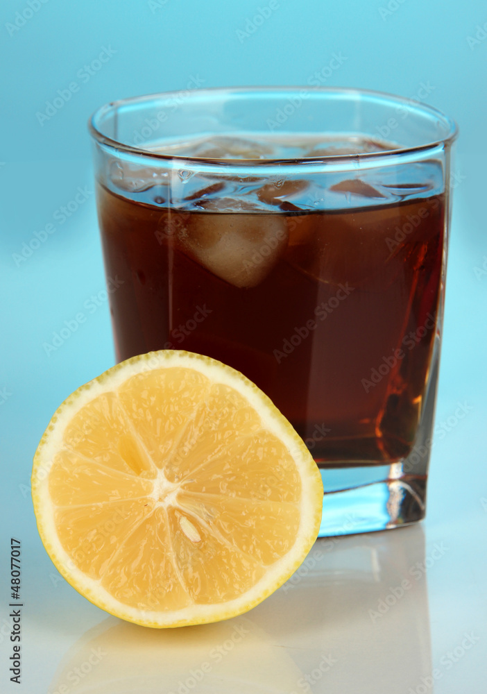 Glass of whiskey with ice and lemon on blue background Glass of whiskey with ice and lemon on blue background