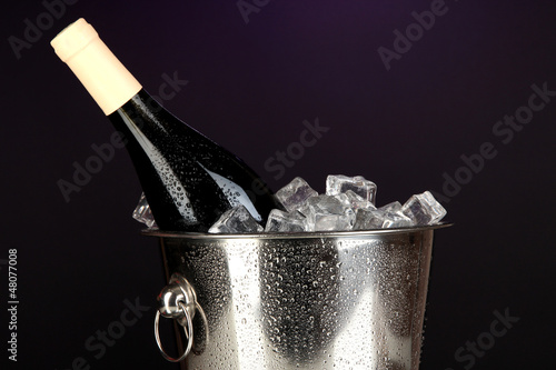 Bottle of wine in ice bucket on darck purple background photo