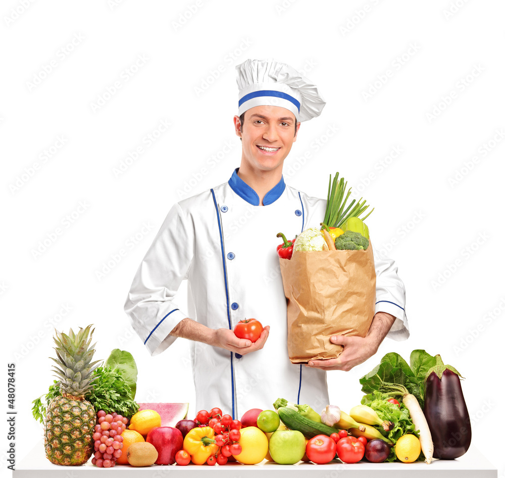 Chef holding a tomato and bag behind a table full of fruits and Chef holding a tomato and bag behind a table full of fruits and