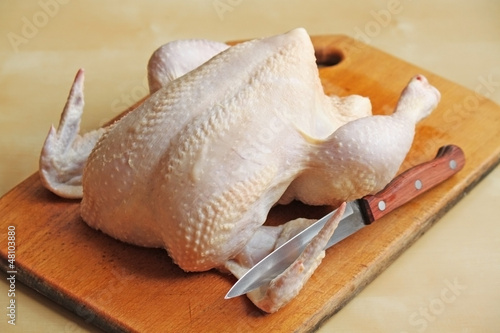Whole raw chicken on the chopping board with a knife