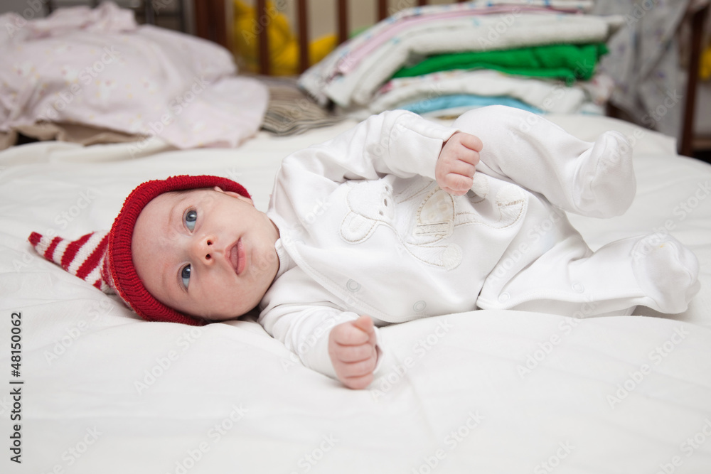 baby in red hat lying on white sheet baby in red hat lying on white sheet
