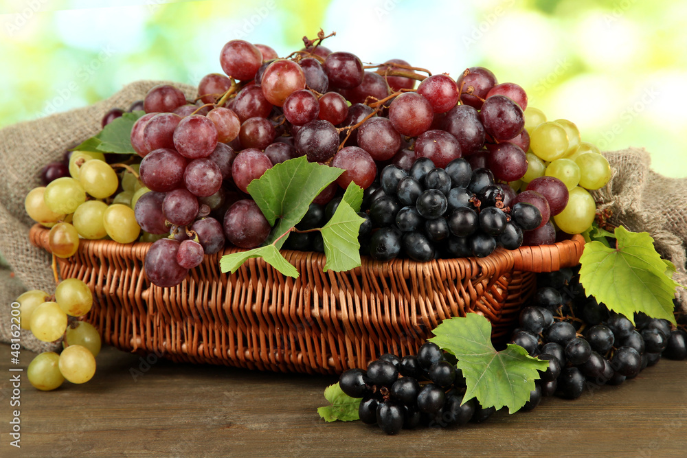 assortment of ripe sweet grapes in basket, on green background assortment of ripe sweet grapes in basket, on green background