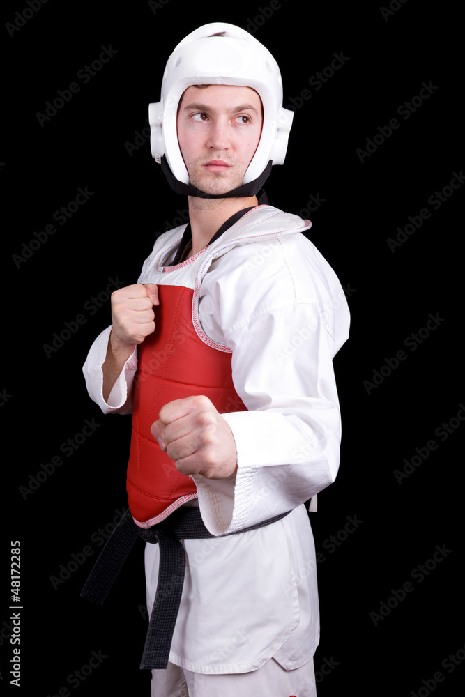 Naklejka premium Young man in Taekwondo gear standing against black background