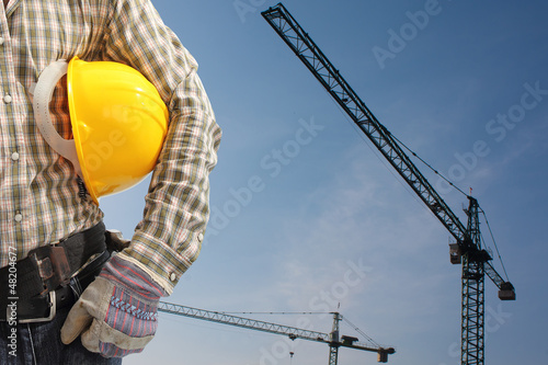 builder worker in uniform and helmet operating with tower crane