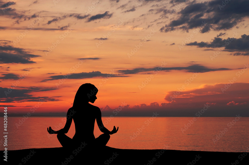 Silhouette of a young woman doing yoga on a sunset background