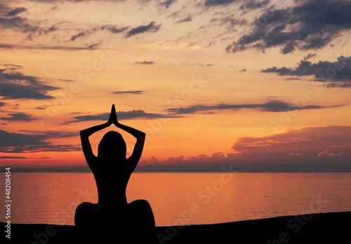 Silhouette of a young woman doing yoga on a sunset background © Acronym