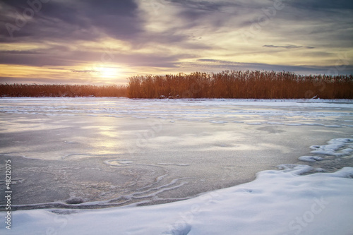 Winter landscape with sun and frozen river.