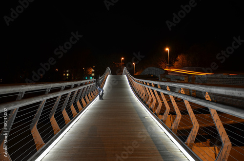 A young woman waits alone on a foot bridge at night.