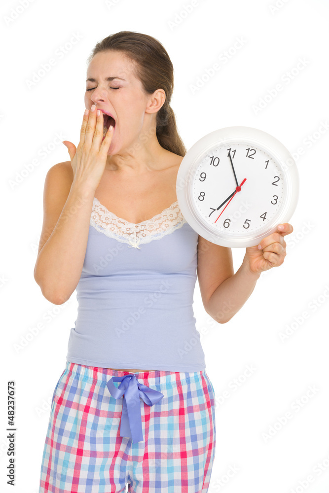 Young woman in pajamas with clock yawing after sleep Young woman in pajamas with clock yawing after sleep