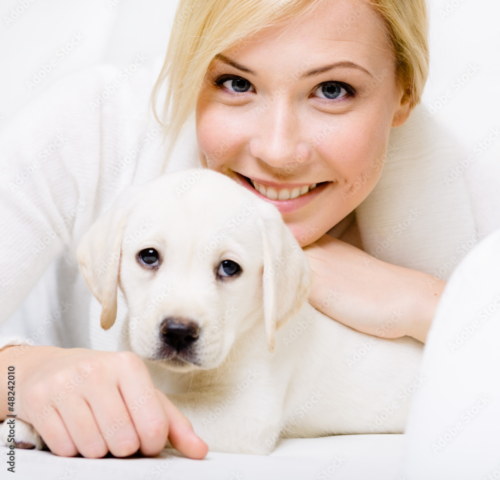 Close up of white puppy of Labrador lying on sofa with woman Close up of white puppy of Labrador lying on sofa with woman