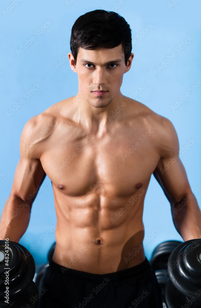 Handsome muscular man with sexy body uses his dumbbell 