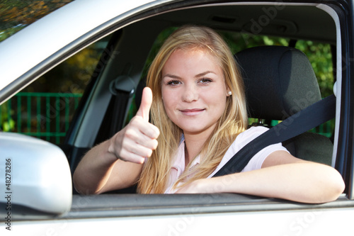 Attraktive junge Frau im Auto zeigt Daumen hoch