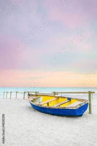 Old yellow blue wooden boat on white beach on sunset