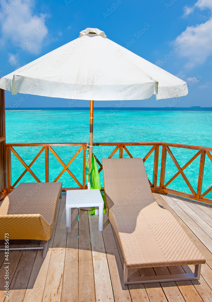 Parasol and chaise lounges on terrace of water villa, Maldives