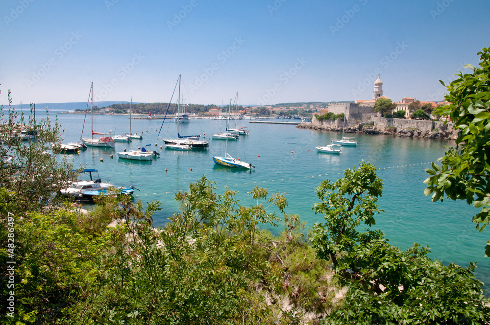Boats on little port beside Krk old town view with vegetation -